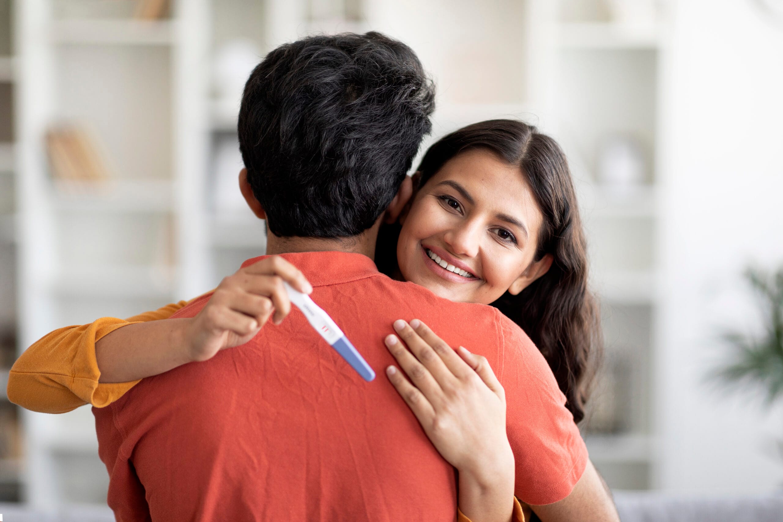 happy indian woman holding positive pregnancy test hugging her husband scaled